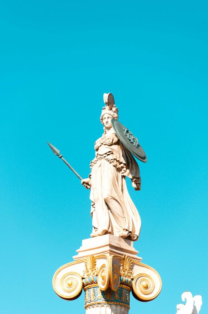 A statue of Athena atop a column. She is holding a shield and a spear while wearing a helmet.