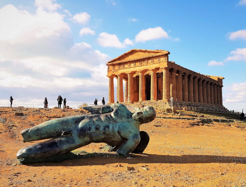 A bronze statue of Ares lying in-front of a temple dedicated to Ares.